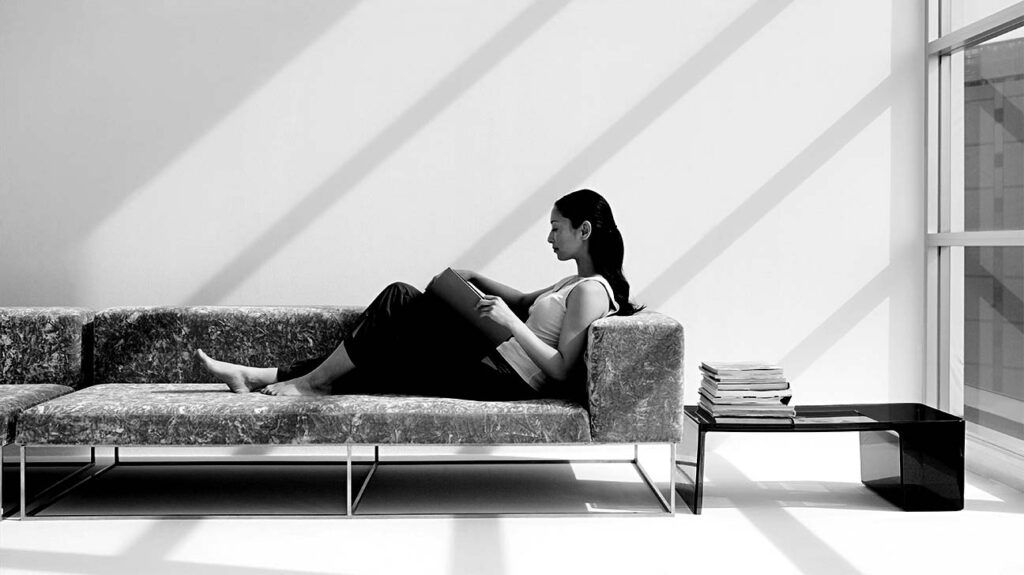 Una donna seduta su un divano con le gambe distese, legge un libro