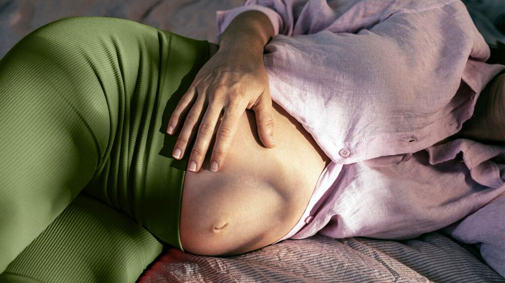 A pregnant person lying on a bed with their hand on their stomach. -1