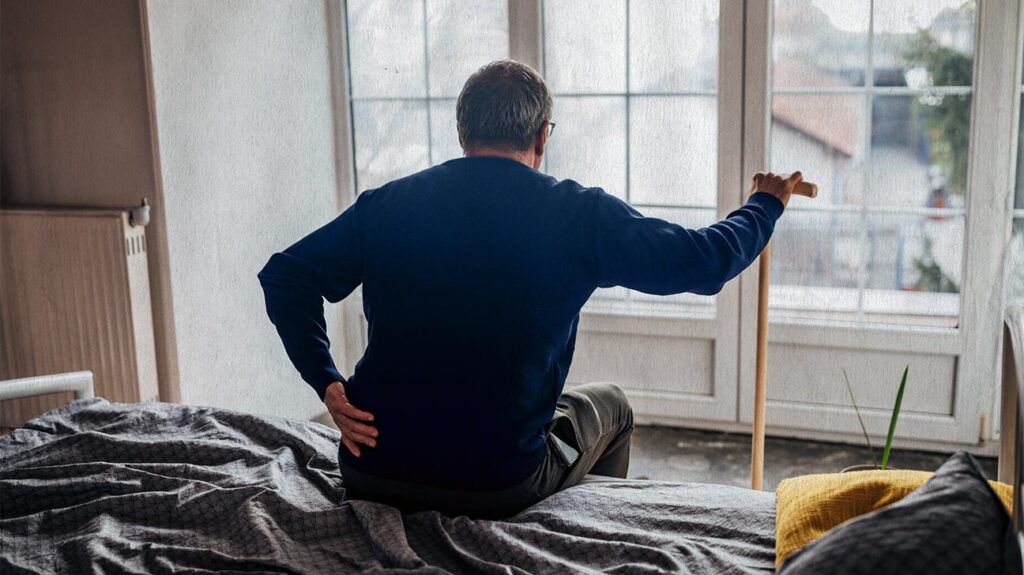 a man is sat on his bed holding his painful back
