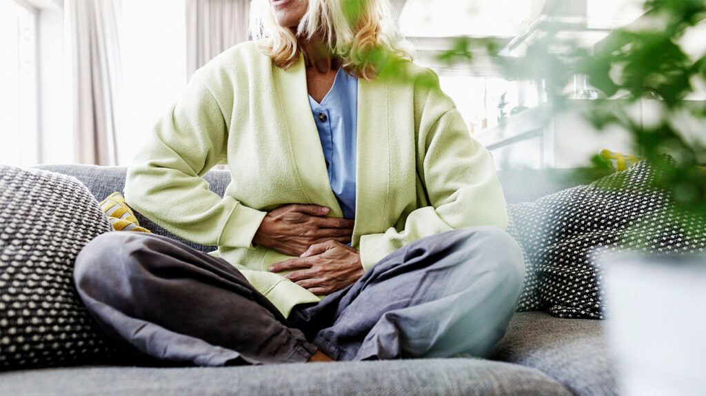 A person holding their stomach sitting on the sofa-1