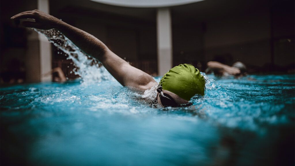 A woman in a green cap swims in a pool