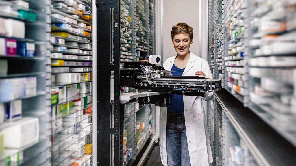 Smiling pharmacist with commissioning machine in pharmacy