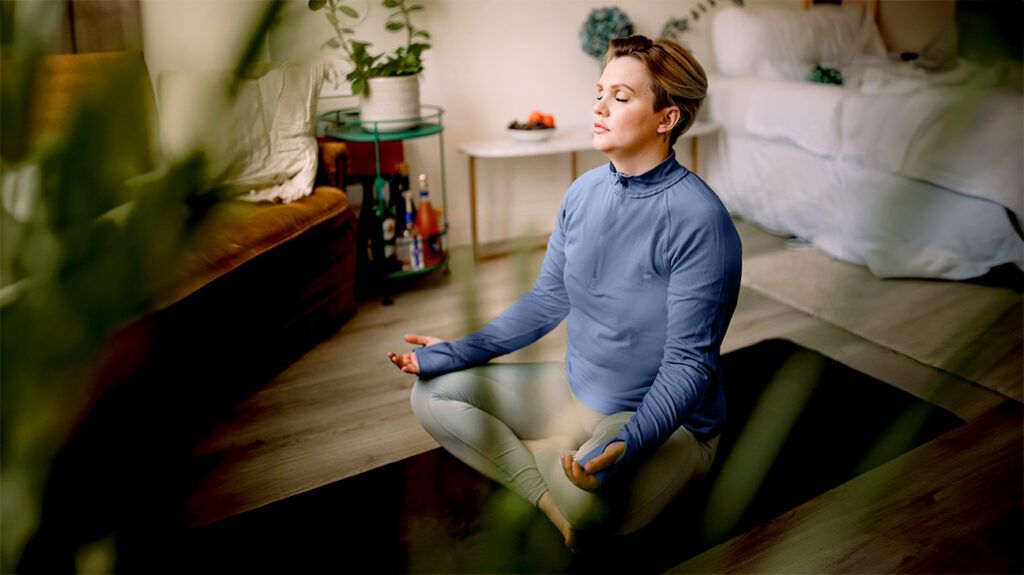 A woman meditates while doing yoga in her bedroomn