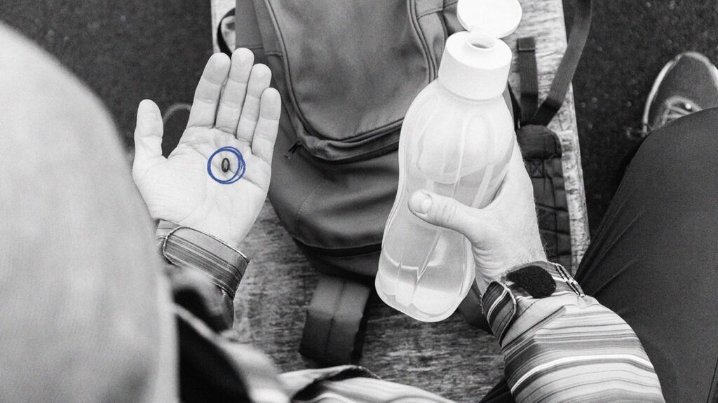 Person holding a pill in one hand and a bottle of water in the other