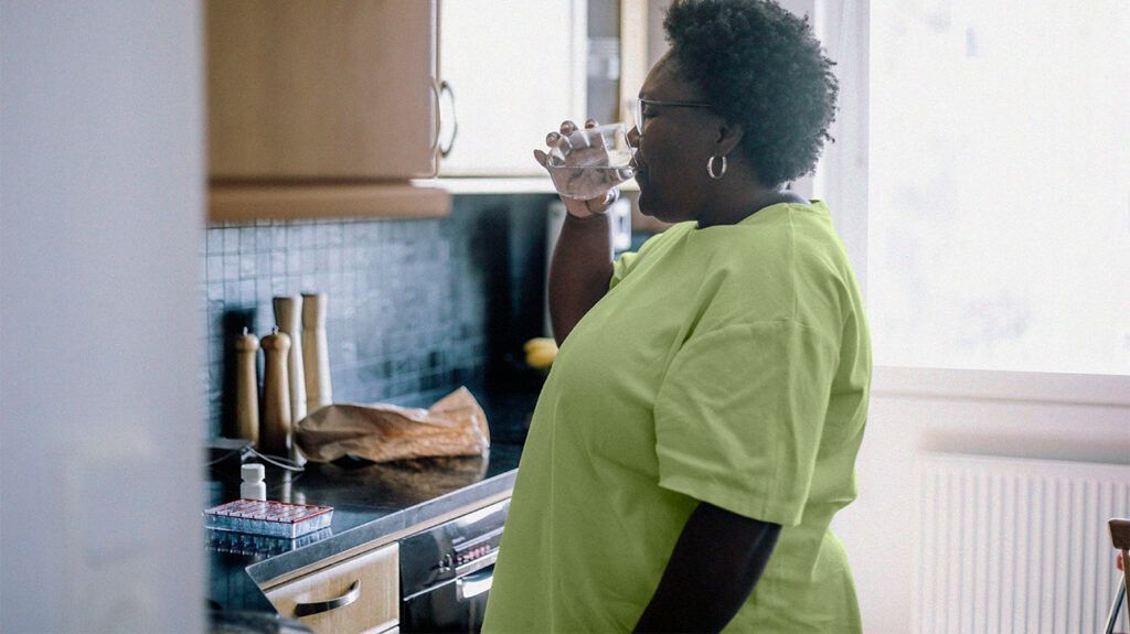 A person is drinking water in a kitchen.
