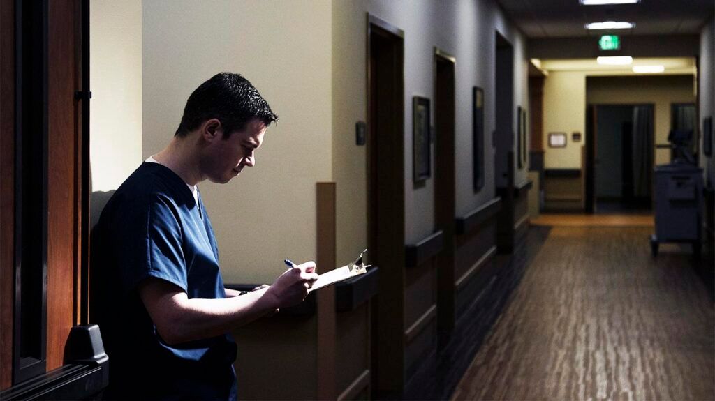 Healthcare professional marking a chart in a hospital corridor