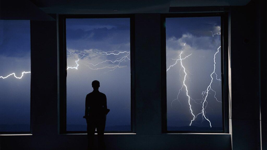 Person standing in front of a window looking at a thunder storm