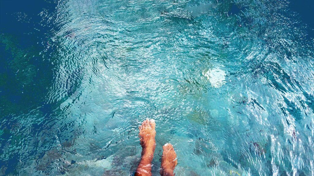 A person's bare feet under clear blue water