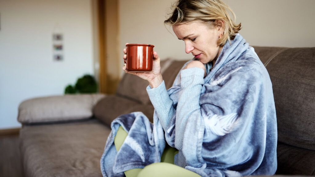 Female sitting on a couch with a mug in her hand, coughing