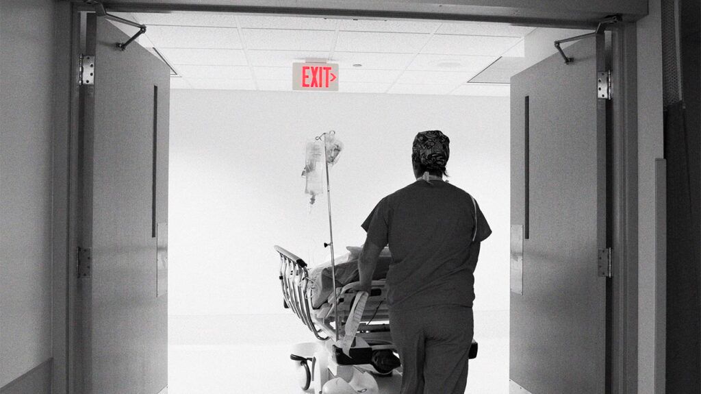 Healthcare professional pushing a bed through a hospital corridor