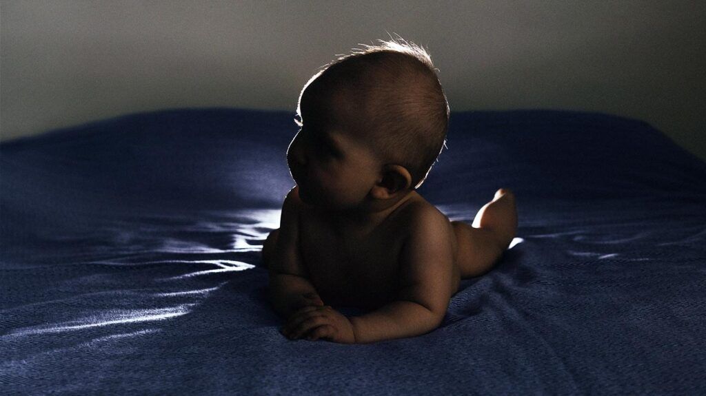 A baby lying in the dark on a mat -2.