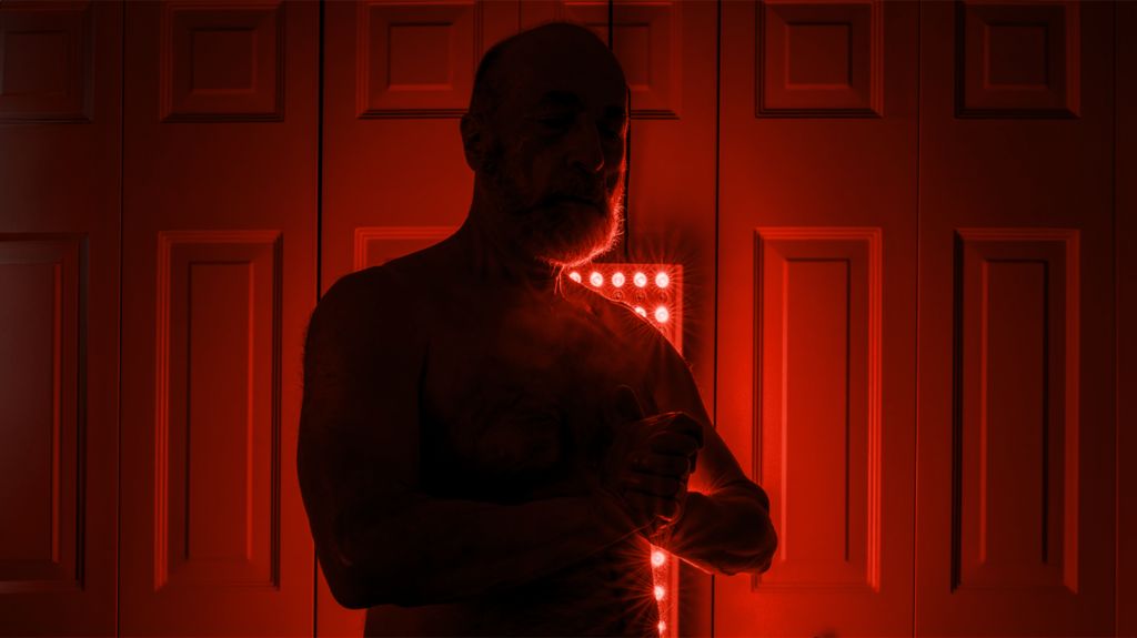 An older man stands while red light fills a room