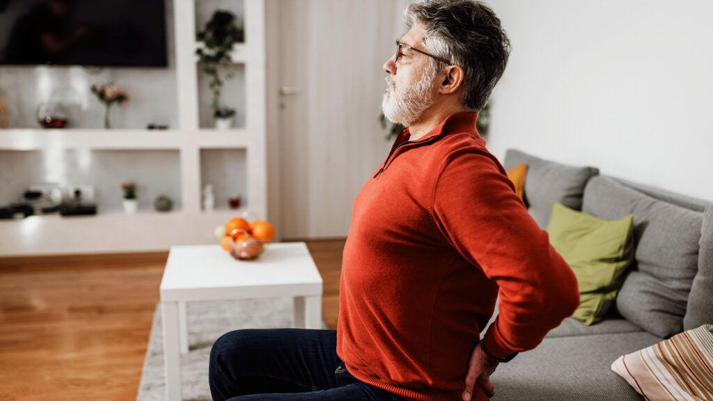 Man in an orange sweater experiencing lower back pain and tightness.