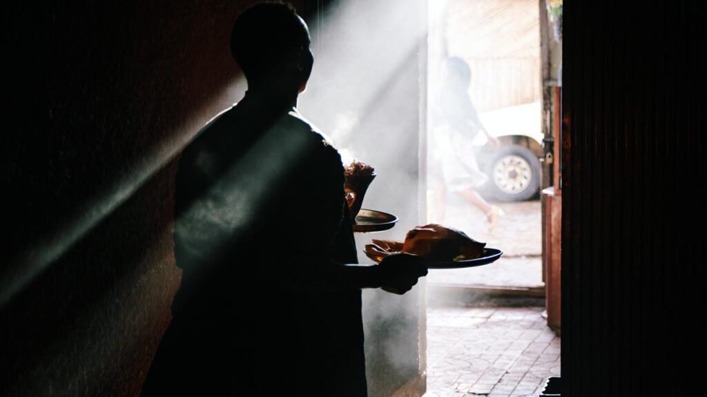 A woman carries plates of food through a dark room