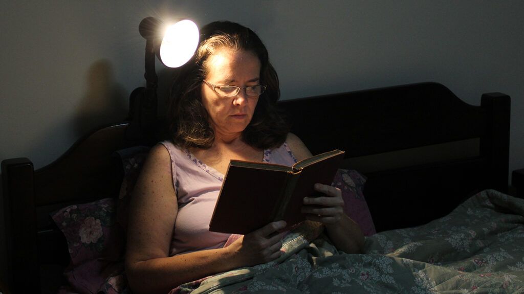 A person reading book in bed at night 2