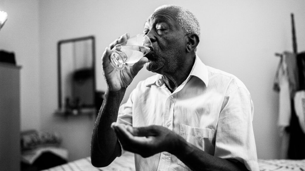 Elder man taking supplements with a glass of water