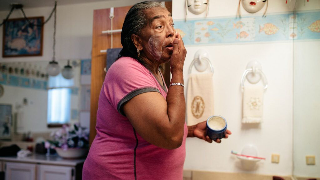Older female putting lotion on her face in a mirror