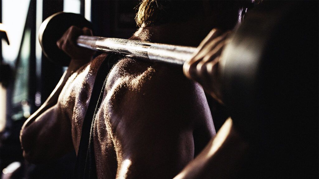 Close up of sweaty weight lifter doing back exercises with a barbell in a gym.