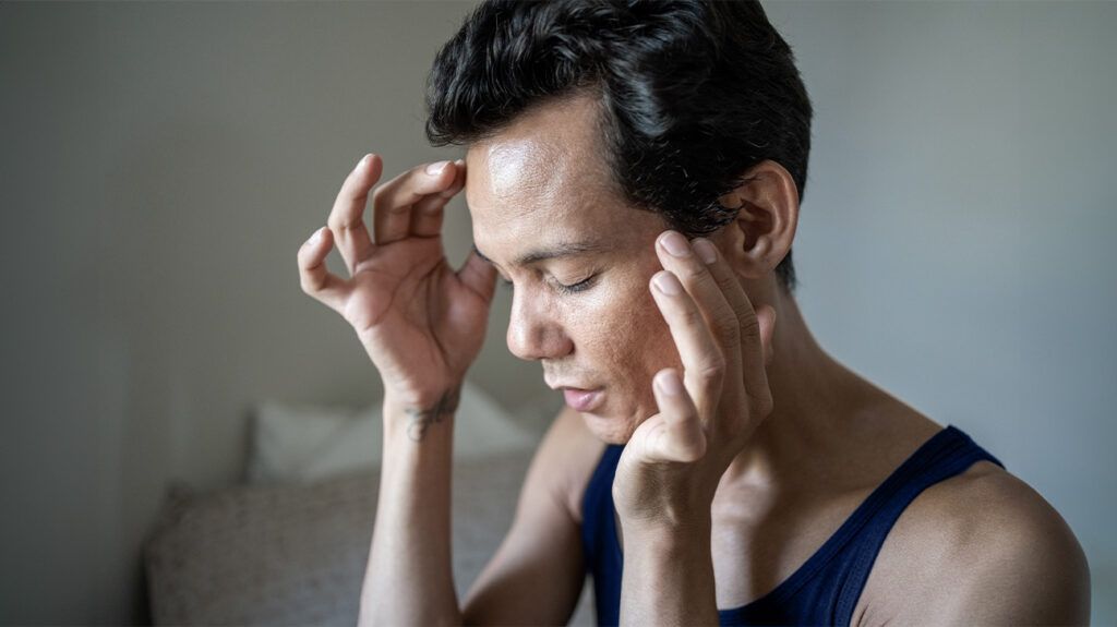 A person touching their face as they have acne that may develop due to progesterone levels -1.