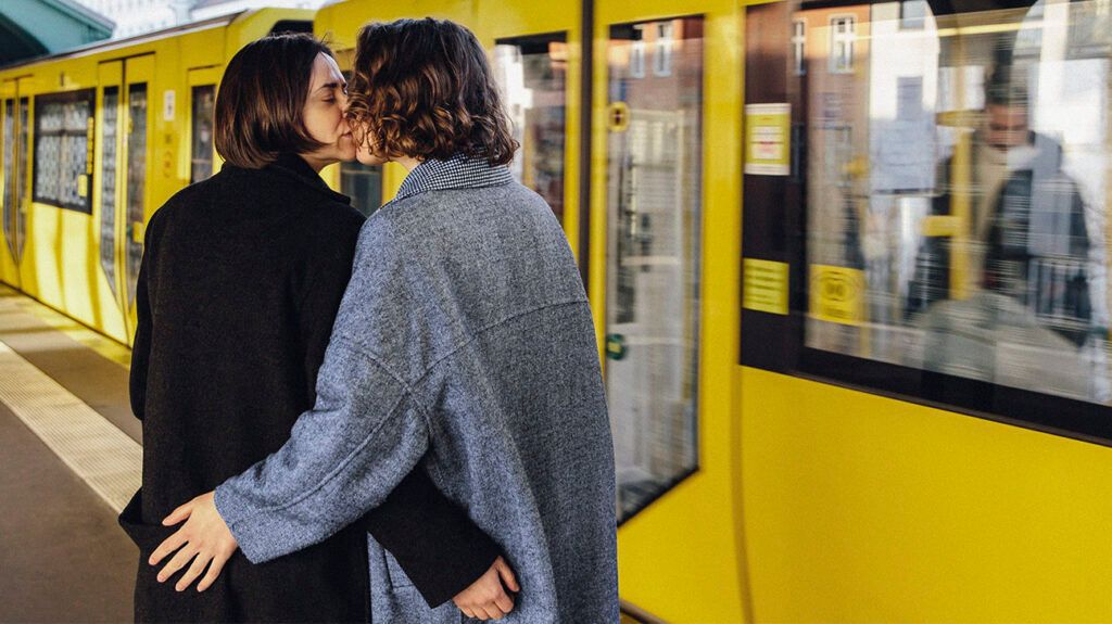 Two people kissing on a platform in front of a yellow train.