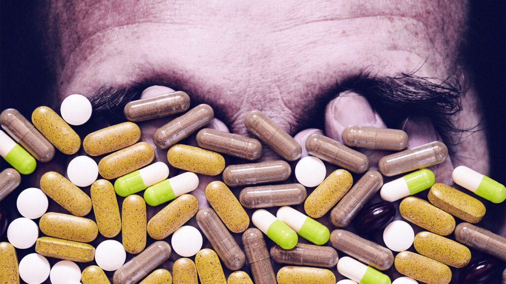 Various pills and medications are scattered in front of a man's face