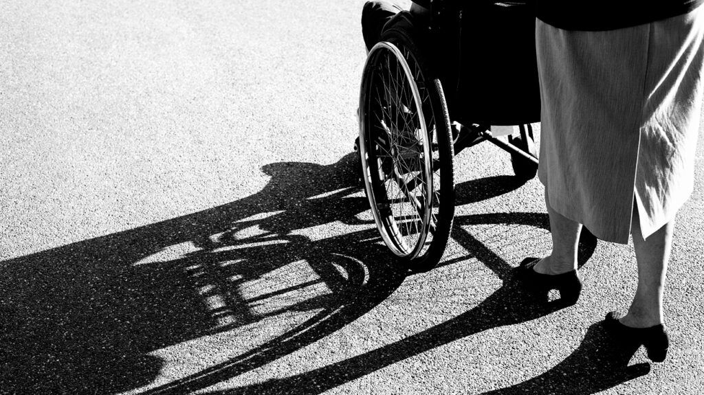 A person with ALS being pushed in a wheelchair -1.