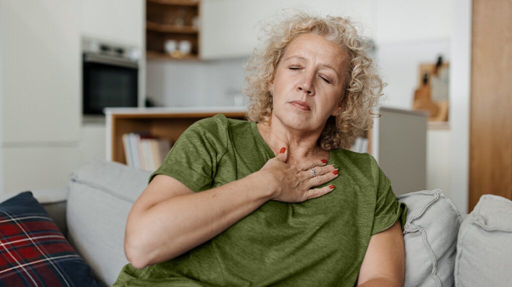A woman on a sofa with her hand on her chest displaying chest pain. -1