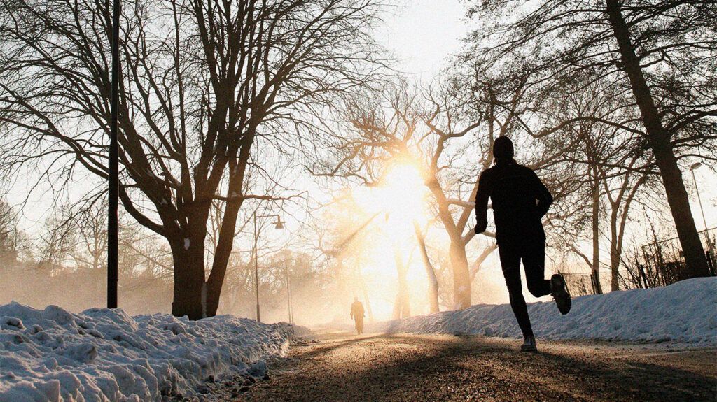 A jogger running in a snowy park at sunrise.
