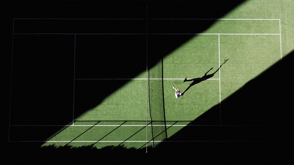 Una ripresa aerea di una partita di tennis dall'alto con l'ombra del giocatore che si riflette sul campo