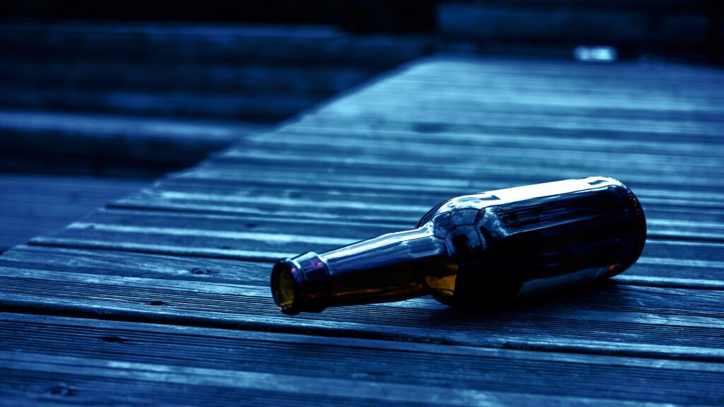 An empty beer bottle on a wooden table at night.