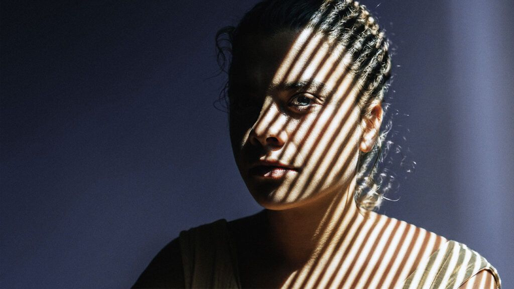 Portrait of a woman sat in partial shade with the shadow of blinds on her face.