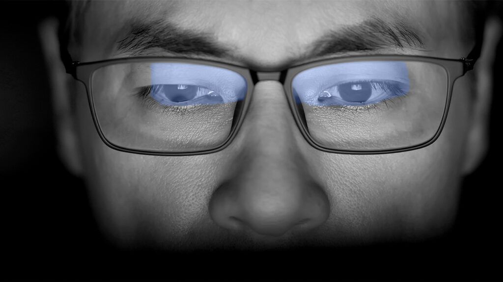 Man wearing glasses with blue light reflection from computer