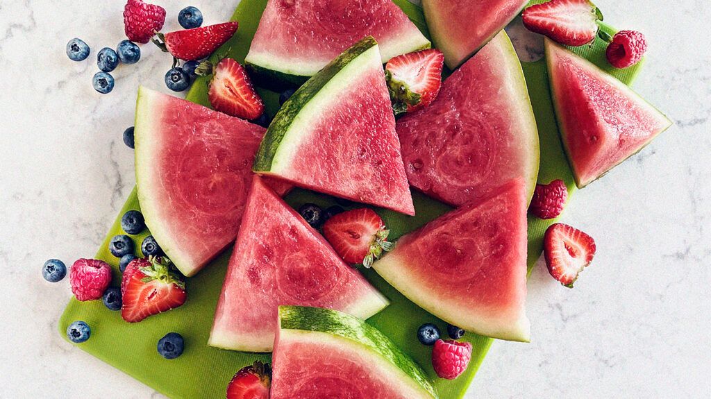 A plate of watermelon slices and berries, which are good foods for relieving gas. -1
