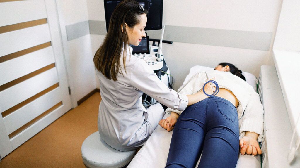 Ultrasound in physical therapy. Young woman therapist using ultrasound scanner on female patient lower back. Back and kidney ultrasound