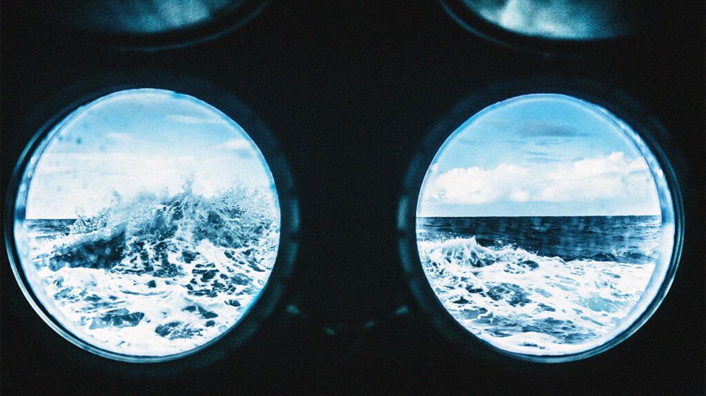 A view of a large wave on an ocean through two porthole windows.-2
