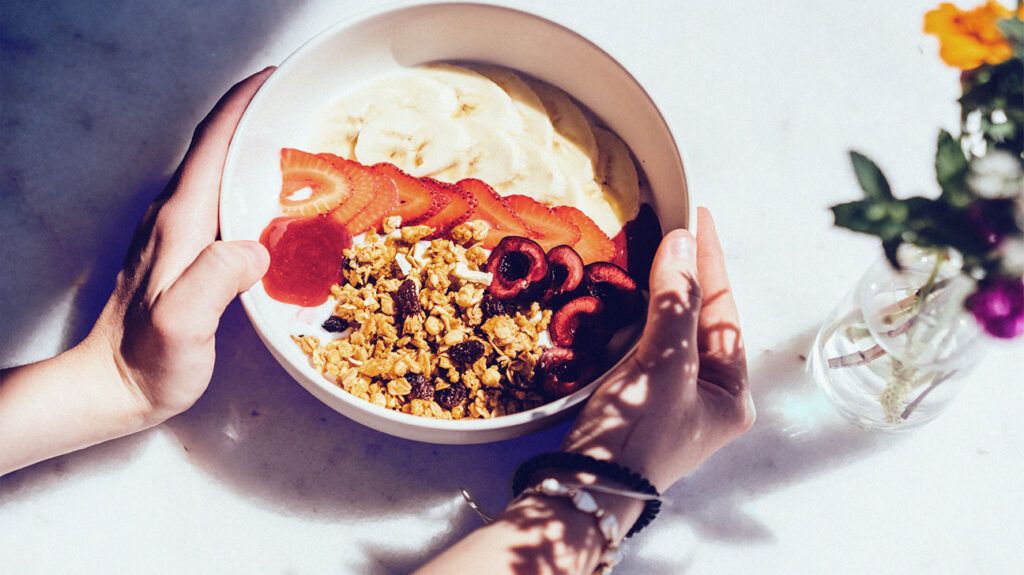 A breakfast granola bowl with cherries, strawberries, and bananas on a bed of yogurt