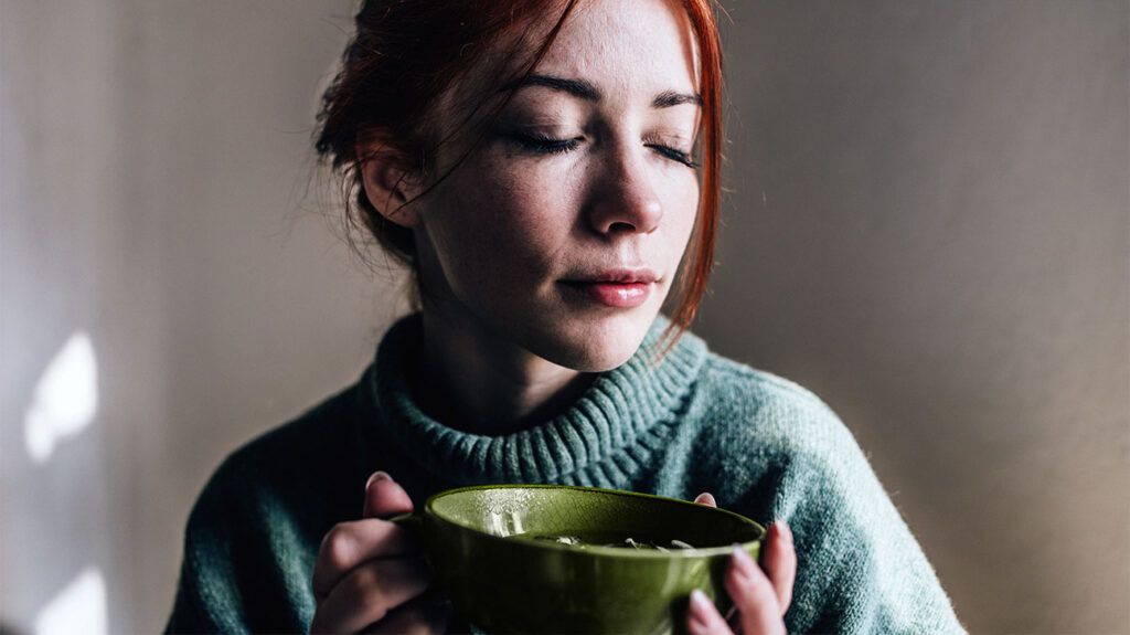 A person is holding a green cup with their eyes closed.