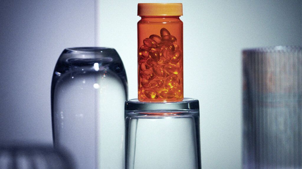 Una bottiglia di vitamine si trova sopra un bicchiere d'acqua
