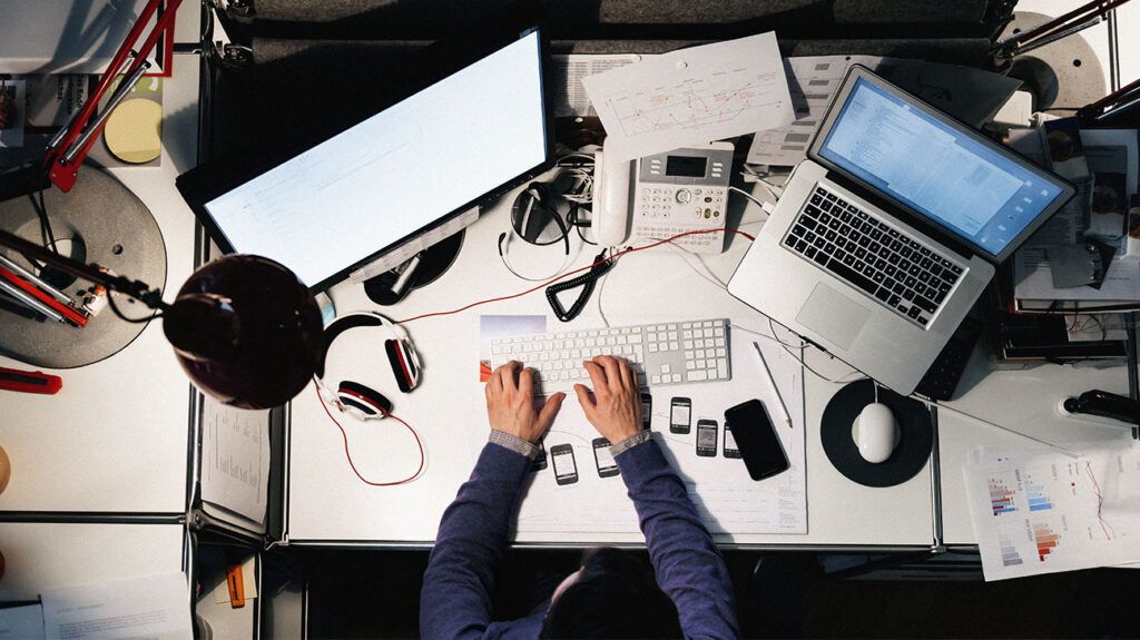 Una vista dall'alto di un uomo che lavora alla scrivania con due schermi attivi