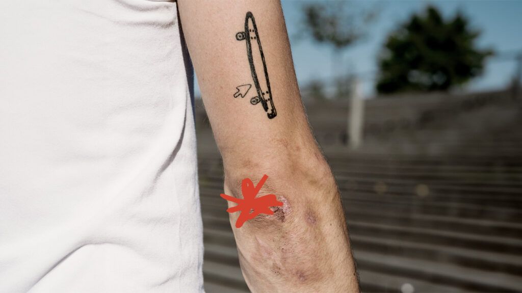 Close-up of a person's elbow with a skateboard tattoo on the upper arm.