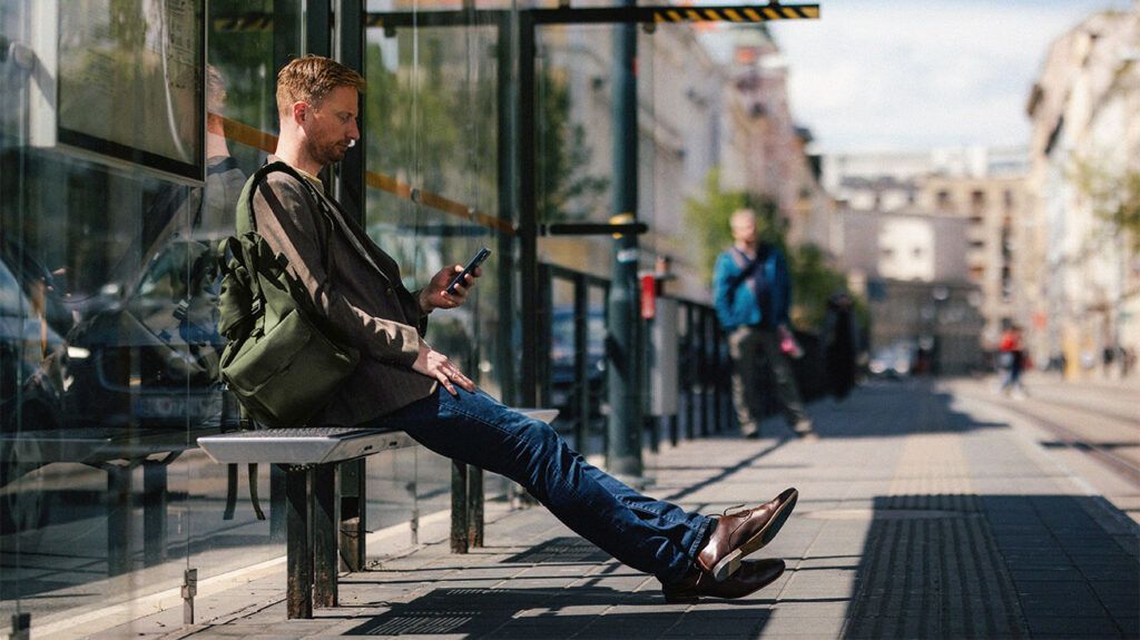 A man is looking at his phone while sitting at a bus stop.