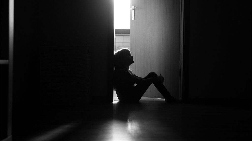 La silhouette di un bambino seduto sulla soglia di una sala buia