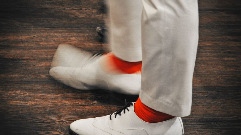 close-up of tapping feet clad in white leather shoes and red socks