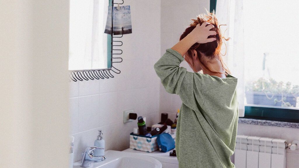 a woman is styling her hair in a bathroom mirror