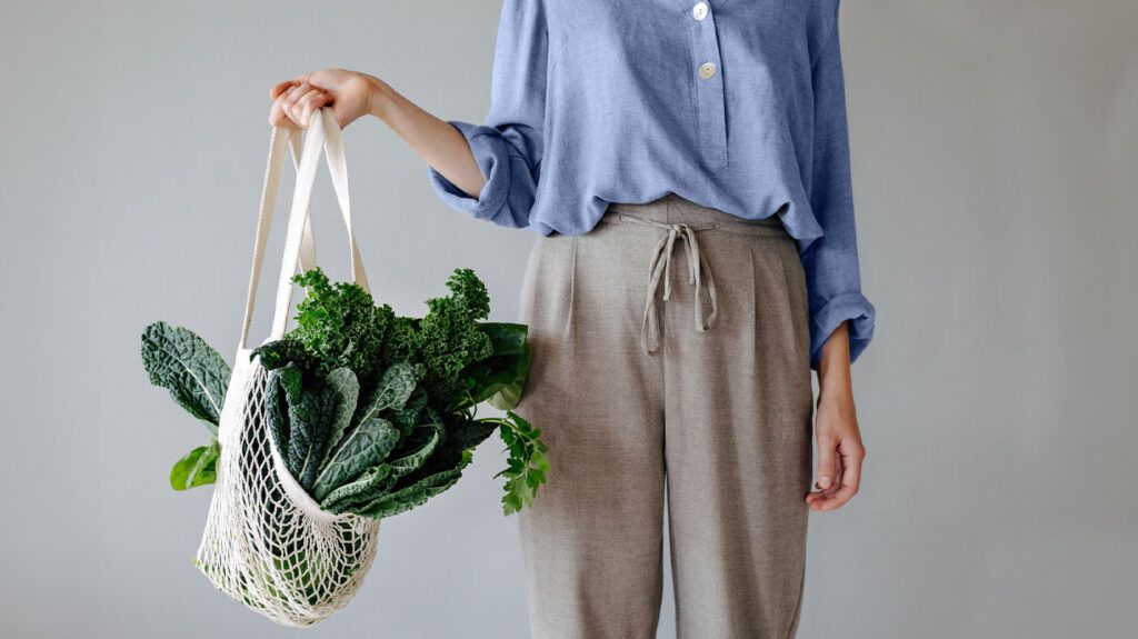 A close up of a woman holding a netted shopping bag full of dark collard greens or cabbage