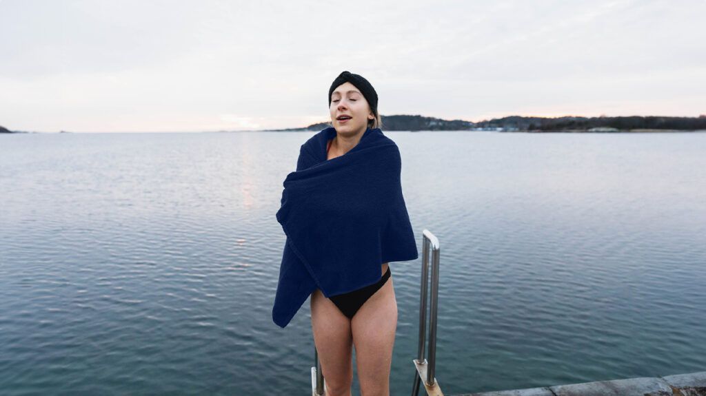 woman emerging from cold water wrapping herself in blue towel