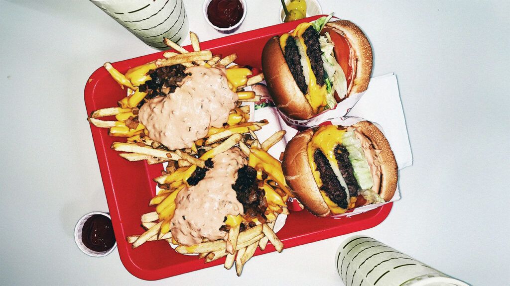 Two double cheeseburgers next to loaded fries on a red tray.