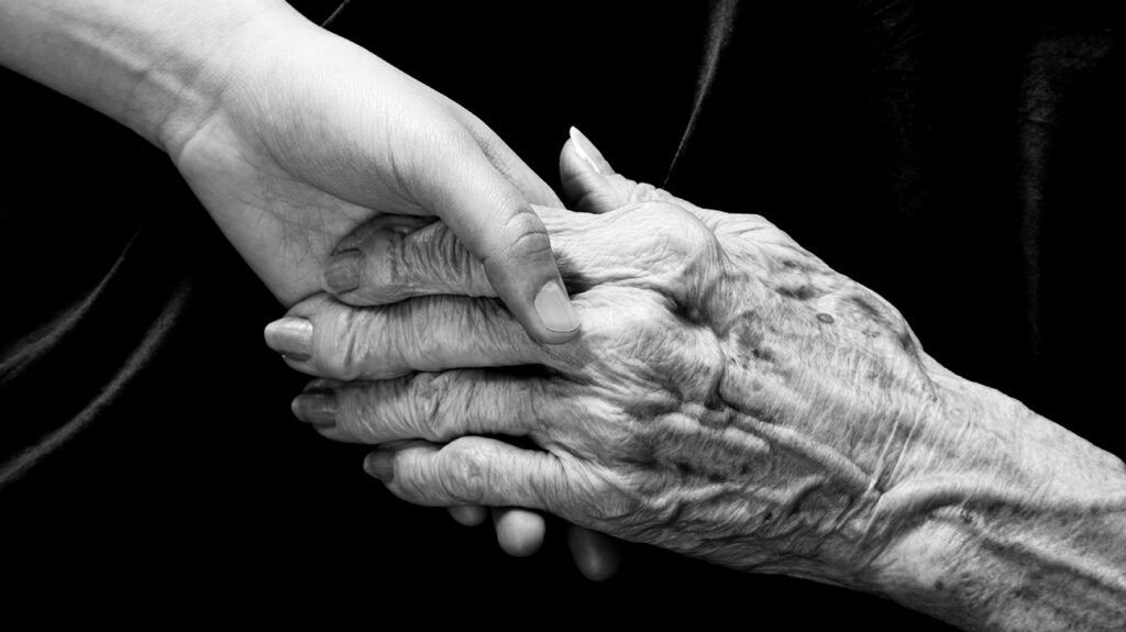 Two people holding hands, one older and one younger, against a black background.