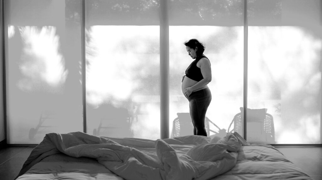A pregnant person holding their stomach in a bedroom.-1