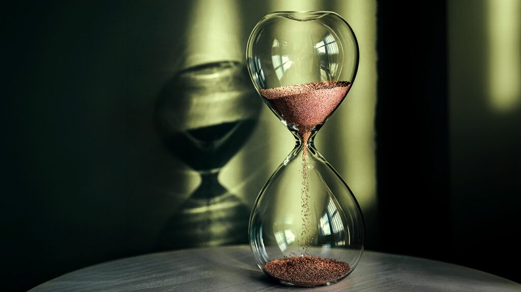 An hourglass is in front of a green background.